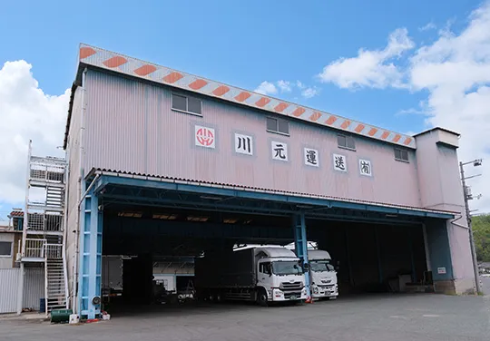 「川元運送」の看板を掲げた社屋と車庫に並ぶトラック