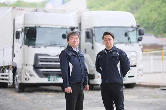大型トラックを背に並ぶ川元運送グループの代表取締役と専務