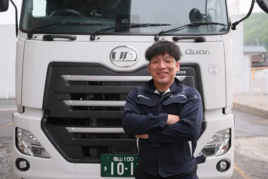 大型トラックの前で笑顔を見せる若手ドライバー